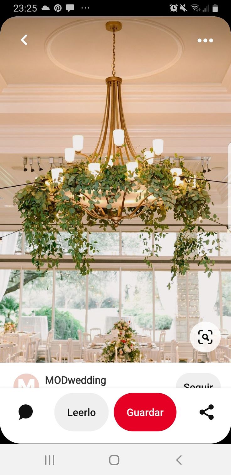 a chandelier hanging from the ceiling with greenery and candles on it at a wedding reception