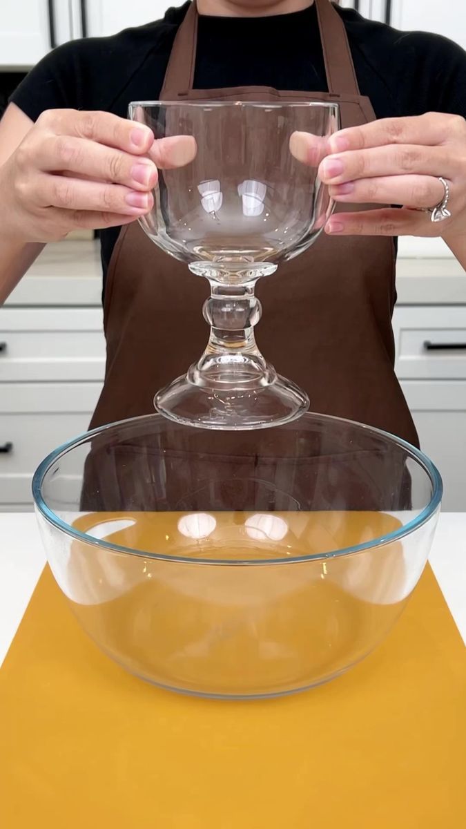 a woman in an apron holding a wine glass over a bowl on top of a counter