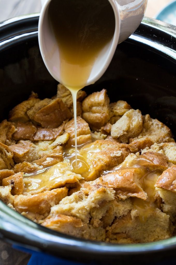 someone pouring caramel sauce into a crock pot filled with bread