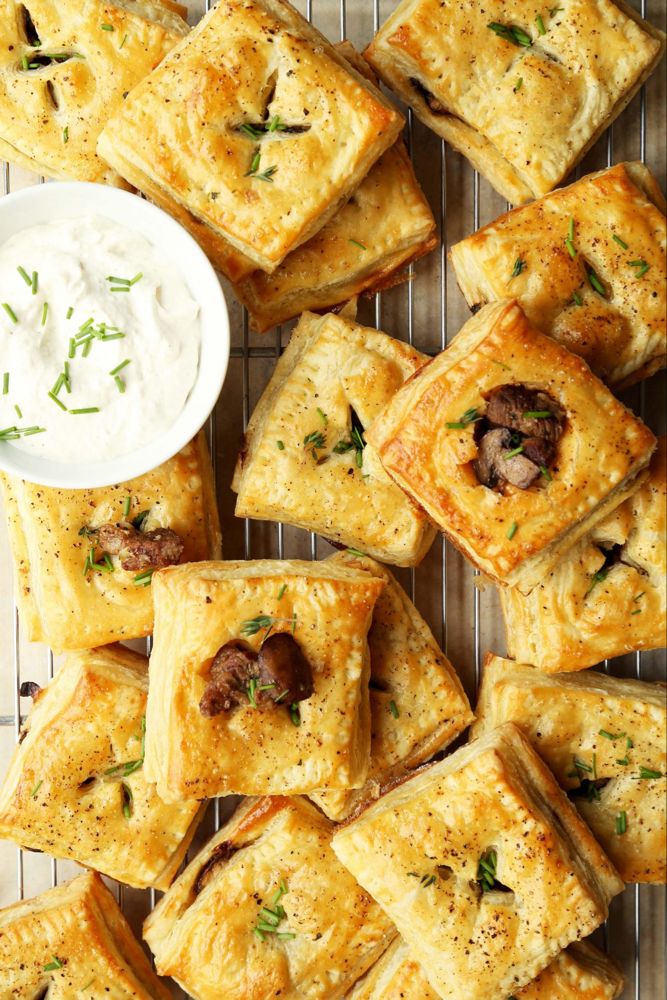 several square pastries on a wire rack with a bowl of sour cream and some herbs