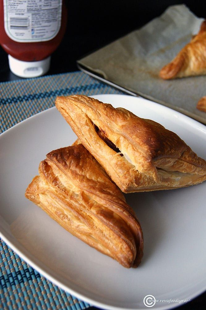 three croissants on a white plate next to a jar of ketchup