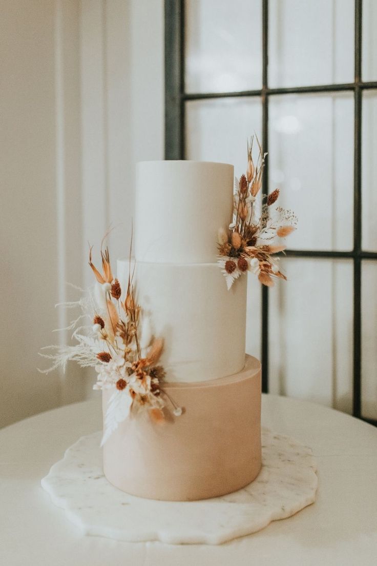 a three tiered wedding cake with dried flowers on top