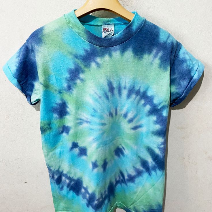 a blue and green tie - dyed shirt hanging on a hanger against a white wall