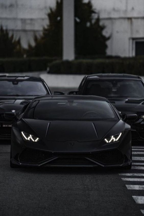 two black sports cars parked next to each other in a parking lot with lights on