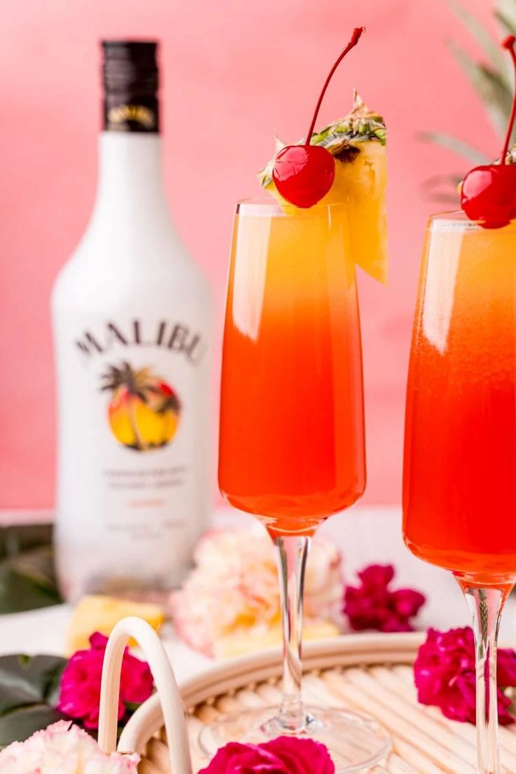 two glasses filled with drinks sitting on top of a table next to bottles and flowers