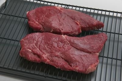 two pieces of steak on a grill being cooked