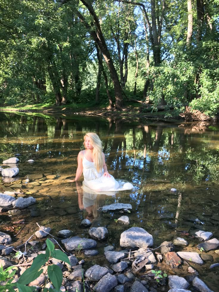 a woman sitting on rocks in the middle of a river with trees and water behind her