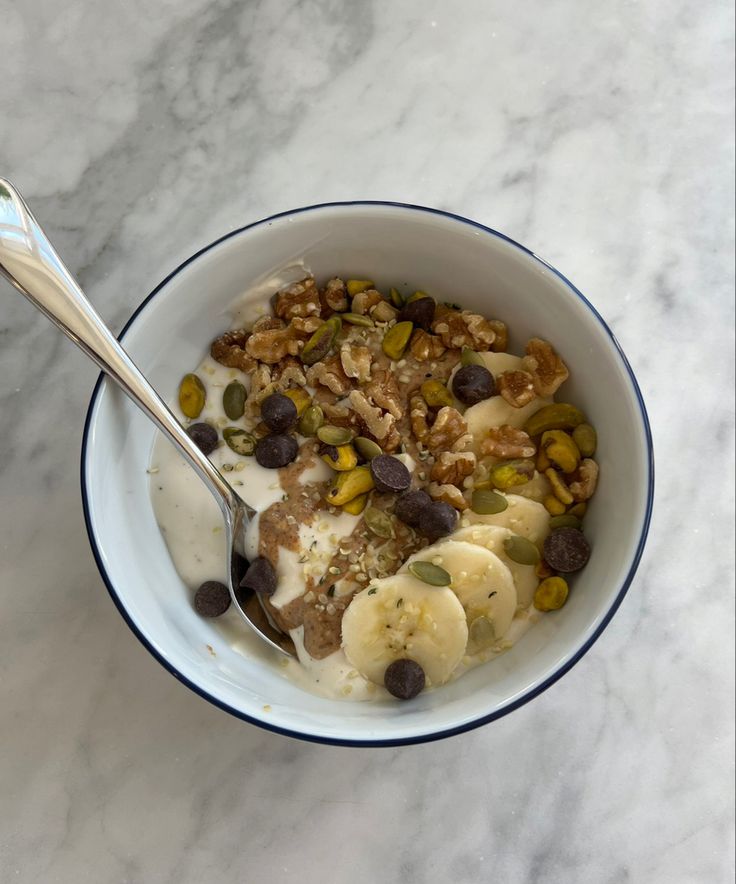 a bowl filled with granola and bananas on top of a marble counter next to a spoon