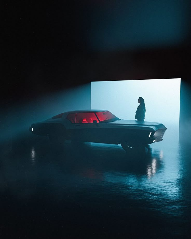 a man standing next to a car in the middle of a foggy room with a large screen behind him