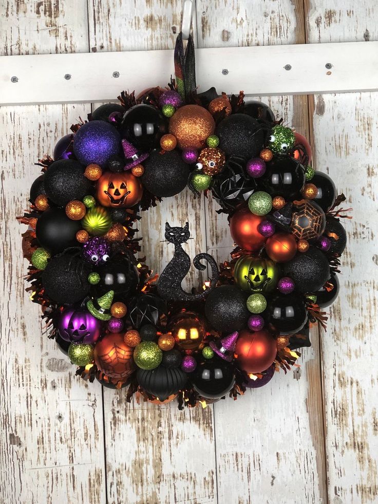 a wreath with black and orange ornaments hanging on a white door hanger next to a wooden plank wall