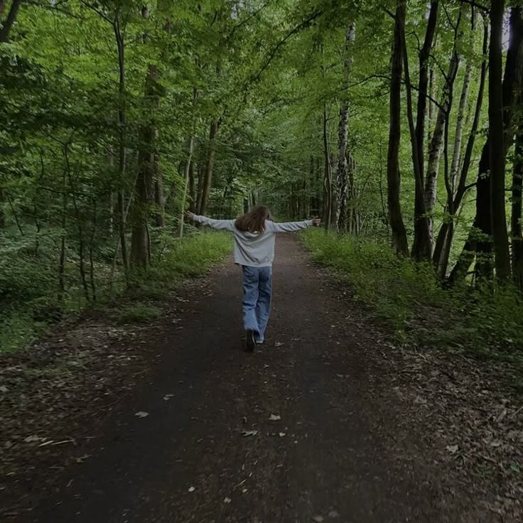 a person walking down a dirt road in the middle of a forest filled with green trees