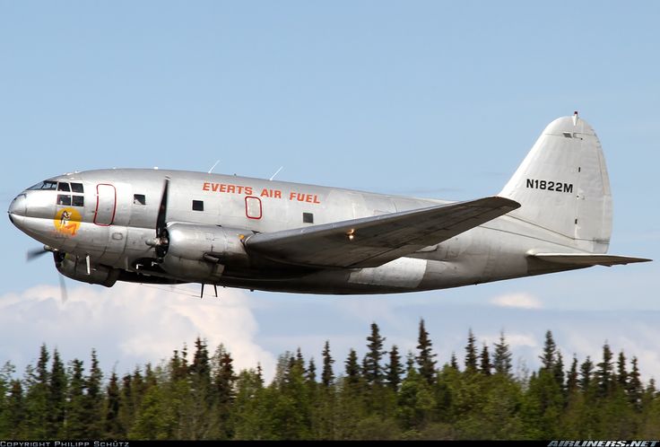 an airplane that is flying in the sky with trees behind it and blue sky above