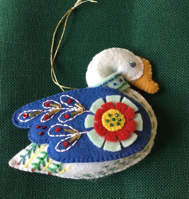 a blue bird ornament hanging on a green cloth covered surface with red, yellow and white flowers