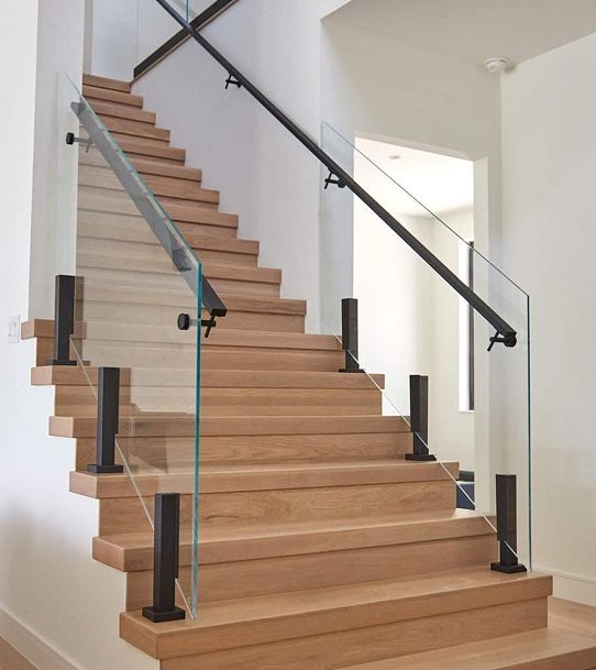 a stair case with glass railing and handrails in a home staircase area that has hardwood floors and white walls