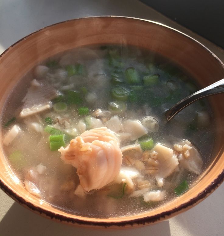 a brown bowl filled with soup and meat on top of a white countertop next to a window