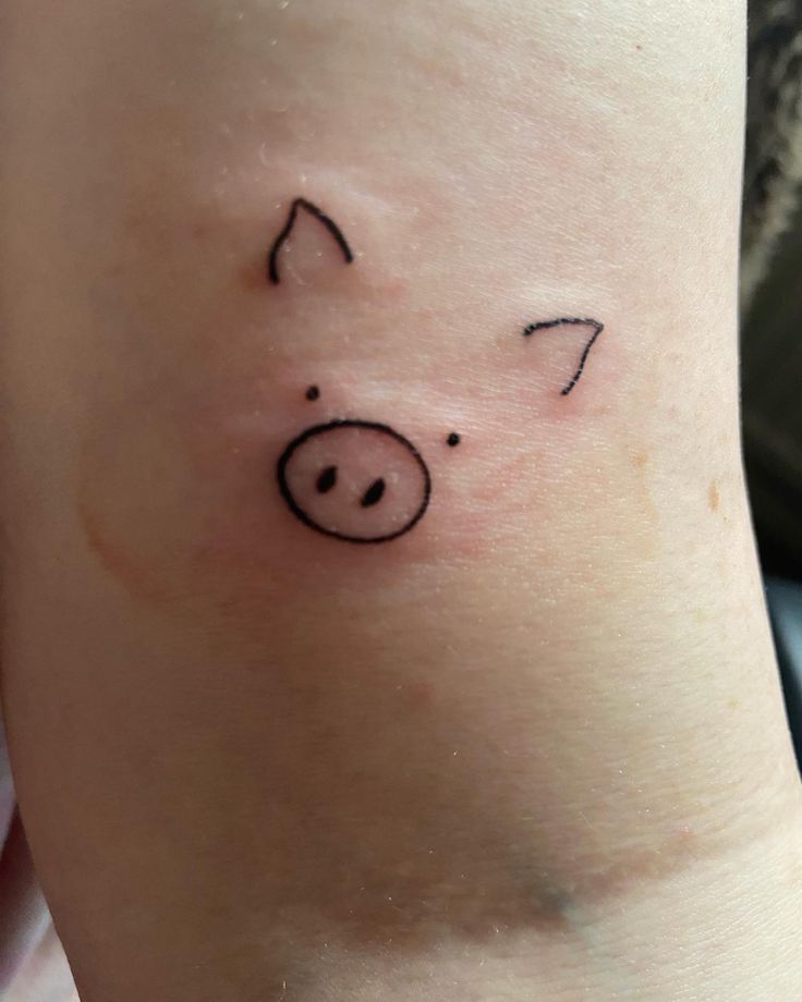 a small pig tattoo on the leg of a woman's arm, with black ink