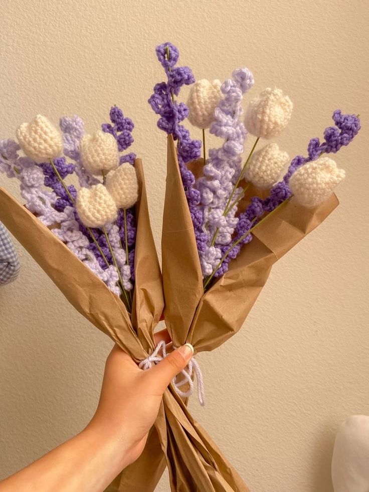 a person holding a bunch of flowers in their hand and wrapped in brown paper with white crocheted balls