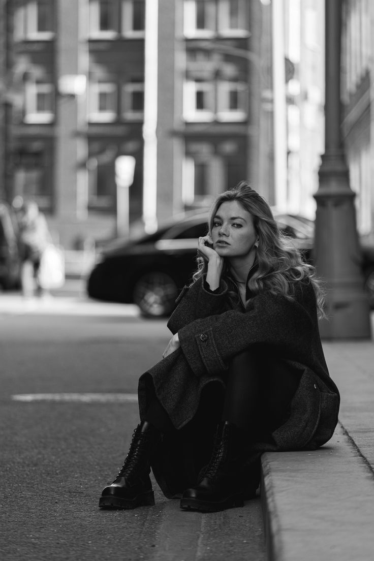 a woman is sitting on the curb with her hand under her chin