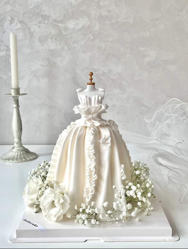 a wedding dress cake sitting on top of a white plate next to a lit candle