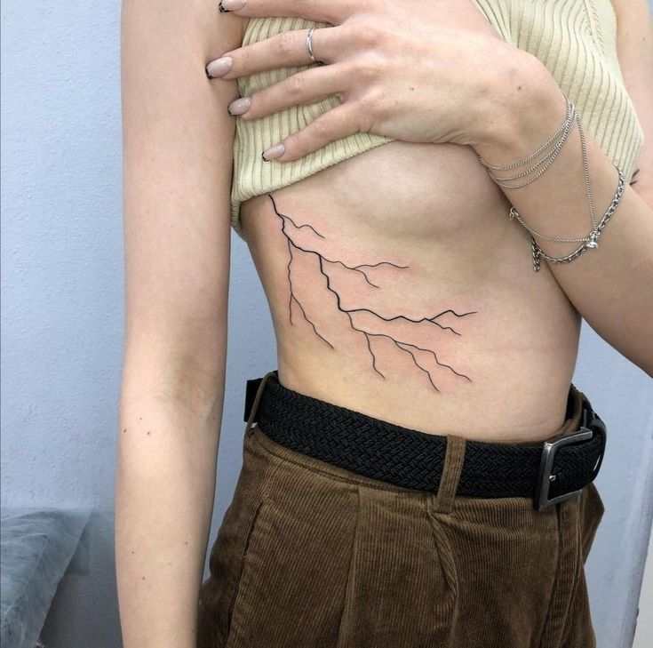 a woman with her hand on the back of her stomach and lightning bolt tattoo on her right side