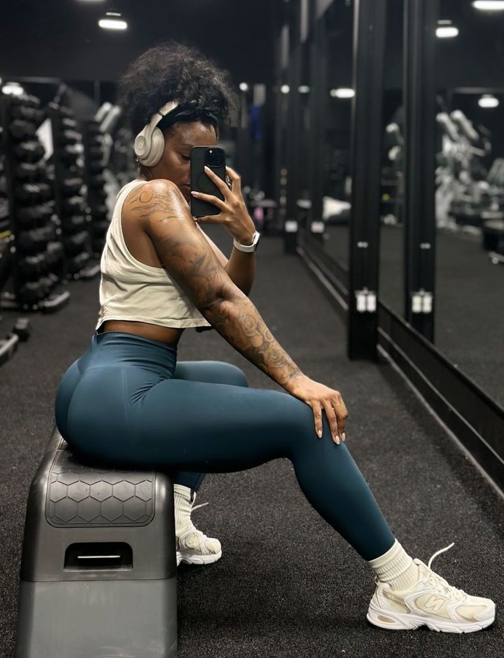 a woman with headphones sitting on a bench in a gym looking at her cell phone