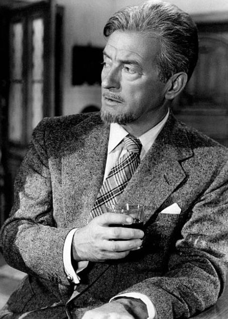 a man in a suit and tie sitting at a table holding a glass with something in it