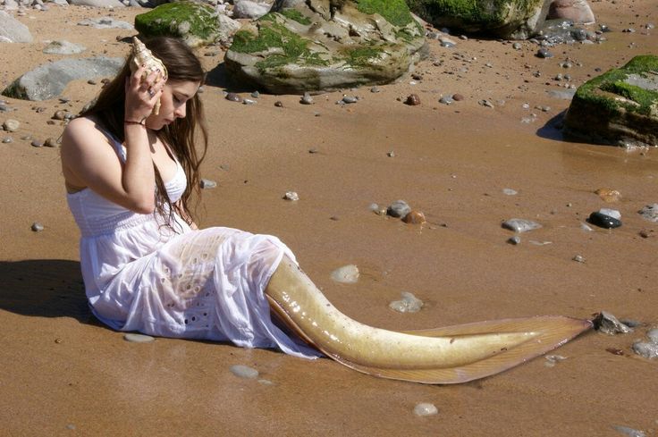 a woman is sitting on the beach talking on her cell phone and wearing a white dress