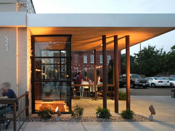 people sitting at tables in front of a building with glass doors and lights on it