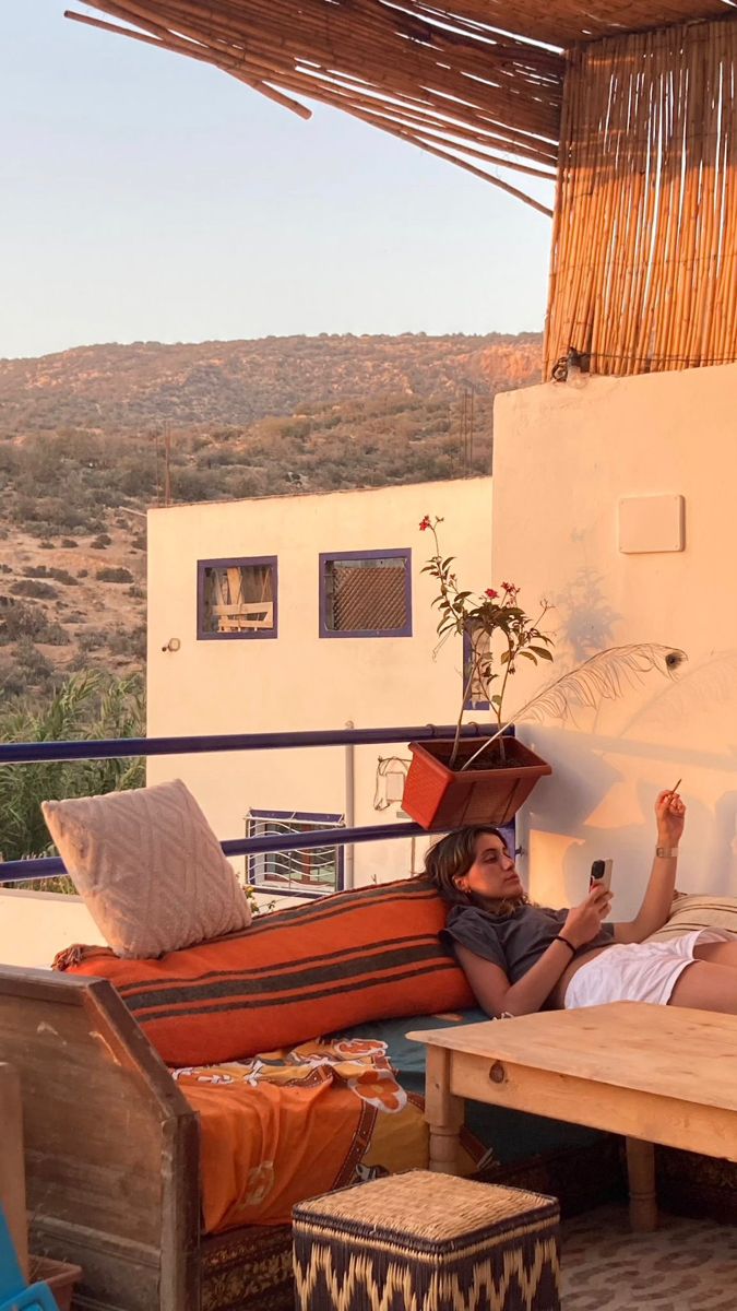 a woman laying on top of a bed next to a wooden table and chair under an umbrella