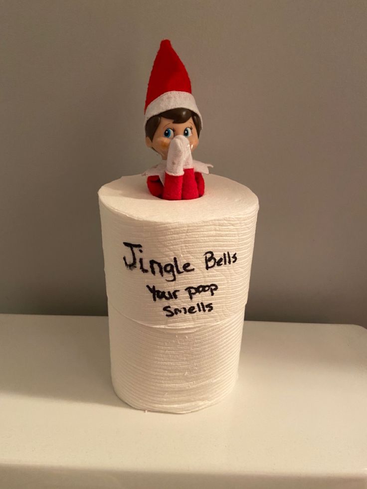 an elf is sitting on top of a roll of toilet paper that says, jingle bells your pop smells