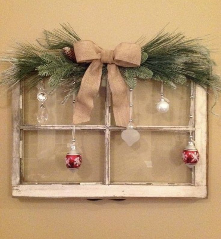 an old window decorated with christmas ornaments and greenery is hung on the wall by a bow