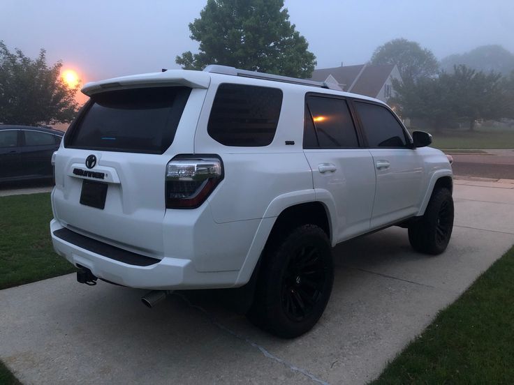 a white suv parked on the side of a road in front of a house at dusk