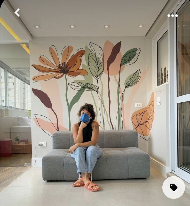 a woman sitting on a couch in front of a wall with flowers painted on it