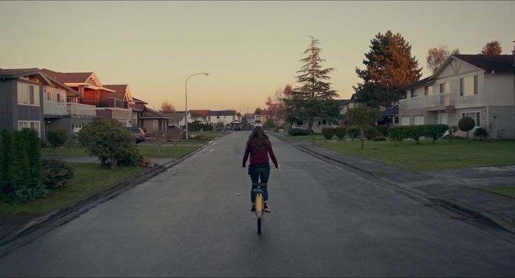 a woman riding a skateboard down a street next to tall houses and trees at sunset