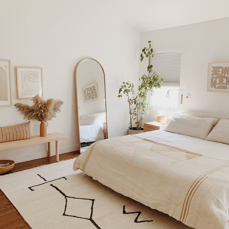 a bedroom with a bed, mirror and plant on the floor in front of it