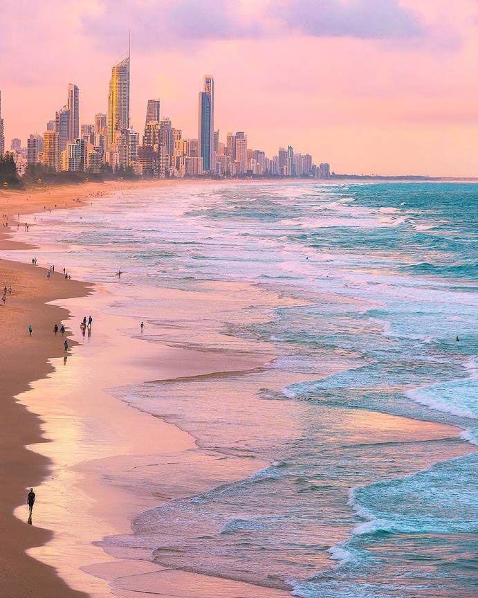 people are walking on the beach in front of an ocean with high rise buildings and skyscrapers