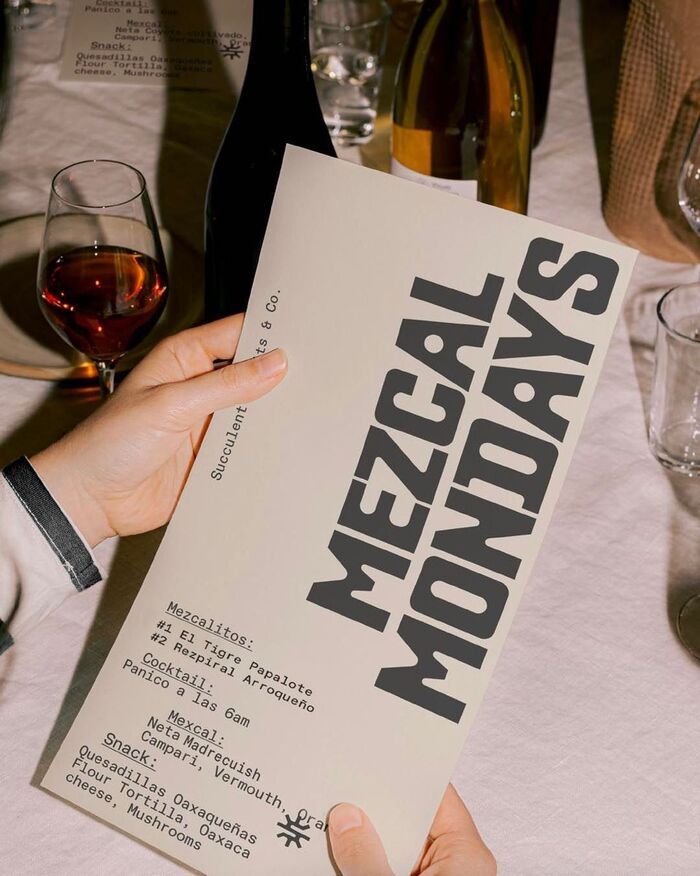 a person holding up a menu at a table with wine glasses and bottles in the background