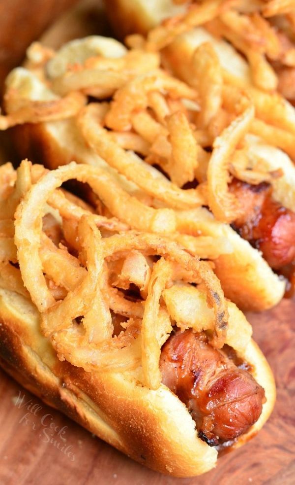 two hot dogs covered in onion rings on a cutting board