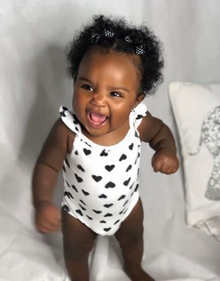 a baby girl in a white bodysuit with black hearts on it's chest