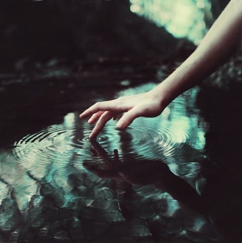 a person's hand reaching for something in the water with their reflection on the surface