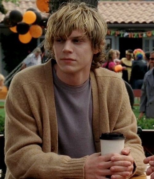 a man sitting at a table with a coffee cup in his hand and people behind him