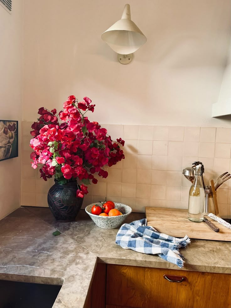 a kitchen counter topped with a bowl of fruit next to a vase filled with flowers