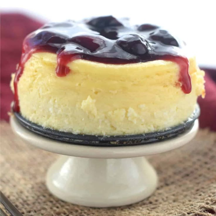 a cheesecake with blueberries and sauce on top is sitting on a cake plate