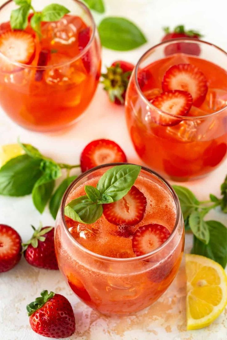 two glasses filled with strawberry lemonade and mint garnish on a white surface