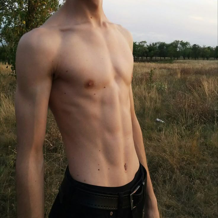 a shirtless man standing in a field with his hand on his hip and looking at the camera