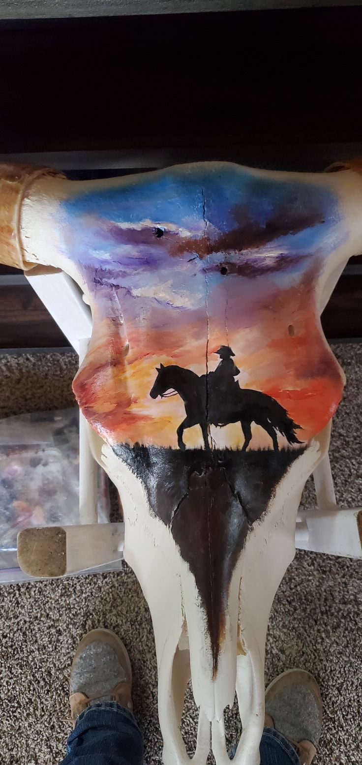 a cow skull with a painting of a horse and rider on it's back