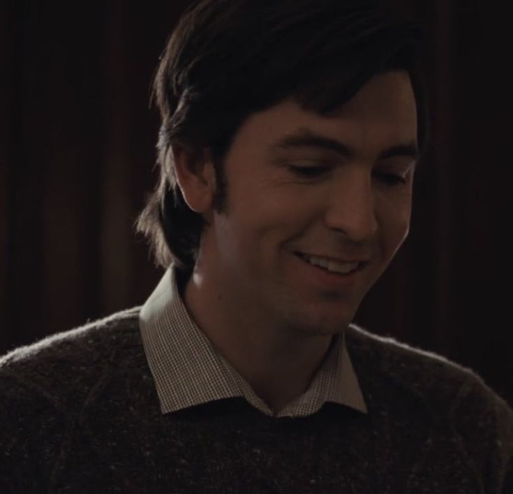 a man smiling and looking at his cell phone in the dark with wood paneling behind him