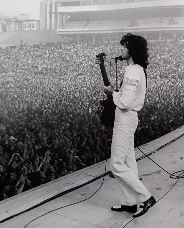 a man standing on top of a stage with a guitar in front of an audience