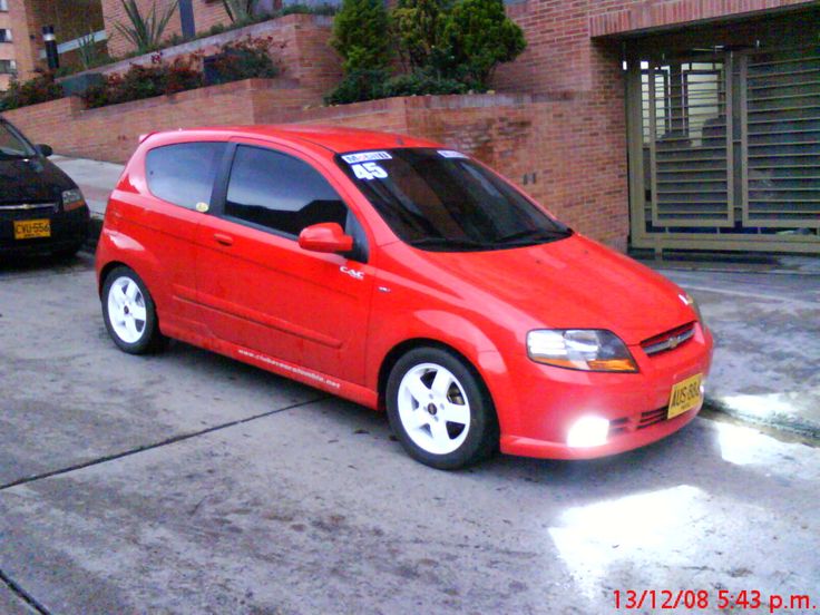 a small red car parked in front of a brick building next to another black car