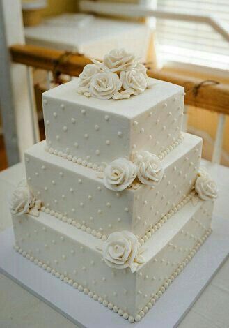 a three tiered wedding cake with white flowers on the side and pearls around the edges